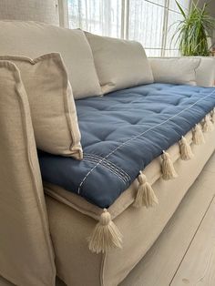 a couch with blue and white pillows on it in front of a large window next to a potted plant