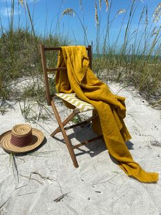 a chair with a yellow blanket on it and a straw hat sitting in the sand