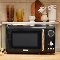 a black microwave oven sitting on top of a counter next to vases and fruit