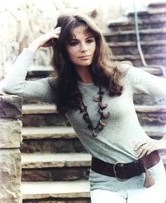 a woman in white jeans and a gray sweater posing for a photo with her hand on her head