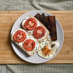 a plate with eggs, bacon and tomatoes on it next to some sliced up meat