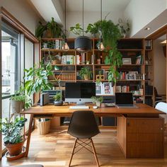 a desk with two computers on it in front of some plants and bookshelves