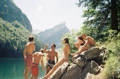 four people are sitting on rocks near the water