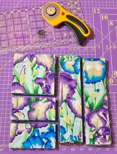 some fabric and scissors are laying next to each other on a cutting board with purple flowers