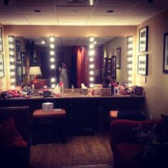 a woman standing in front of a bathroom mirror with lights on the side of it