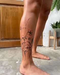 a close up of a person's leg with flowers on it and a plant in the background