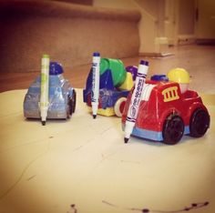 two toy cars sitting on top of a table next to crayons and markers