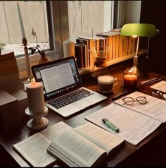 an open laptop computer sitting on top of a wooden desk next to books and glasses