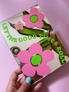 a person holding up a pink and green flower sticker on a card that says let the good times roll