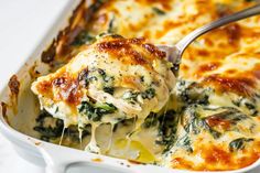 a casserole dish with spinach and cheese being scooped from the casserole