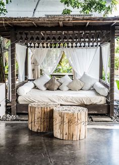 a canopy bed sitting under a tree next to a white couch and table with pillows on it