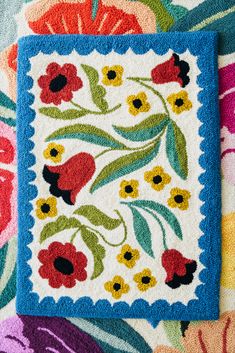 an embroidered square with flowers on it sitting on top of a colorful blanket and pillow