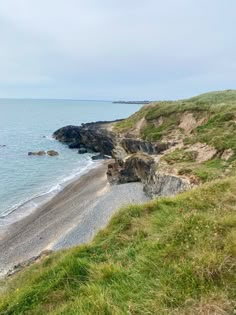 an empty beach on the side of a cliff near the ocean with green grass and rocks