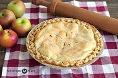 an apple pie sitting on top of a checkered table cloth next to some apples