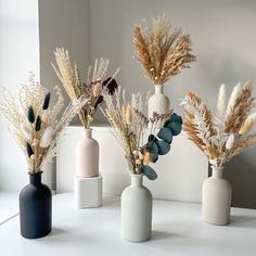 three vases with dried plants in them on a table