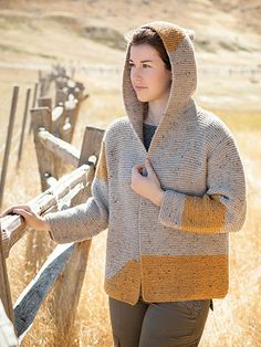 a woman wearing a hoodie standing in front of a fence with her hands on her hips