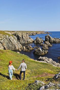 two people holding hands while walking up a hill next to the ocean