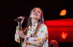 a woman with long hair holding a microphone in her hand and singing into the air