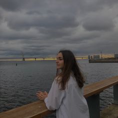 a woman is standing on a bridge overlooking the water