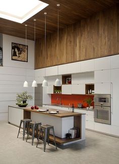 an open kitchen with white cabinets and wood ceilinging, along with bar stools