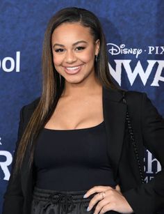 a woman with long hair wearing a black dress and blazer smiling at the camera