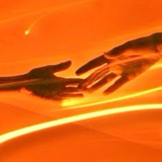 a pair of hands reaching for something in an orange bowl with light coming through it