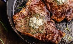 two steaks in a cast iron skillet on a wooden table with herbs and seasoning