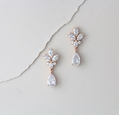 two pairs of diamond earrings sitting on top of a white surface