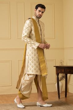 Light gold dupion silk sherwani with mandarin collar, all over floral butti pattern and zardozi hand embroidery.
Components: 1
Pattern: Hand Embroidered
Type Of Work: Zardozi Work
Neckline: Mandarin Collar
Sleeve Type: Full Sleeves
Fabric: Dupion Silk
Color: Gold
Other Details: 
Front and side slits
Closure: Front concealed placket
Note: The dupatta and dhoti worn by the model is not for sale
Occasion: Groom,Wedding - Aza Fashions Dhoti Sherwani, Embroidered Sherwani, Zardozi Work, Sherwani For Men, Men's Ethnic Wear, Diwali Sale, Dhoti Pants, Dupion Silk, Gold Border