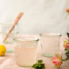 a table topped with glasses filled with liquid next to lemons and flowers on top of a table