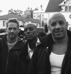 three men standing next to each other in front of parked cars