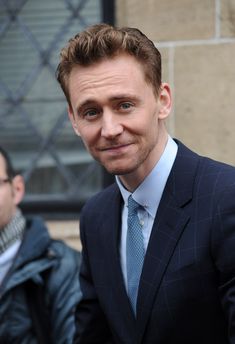 a man in a suit and tie smiles for the camera while standing next to a building