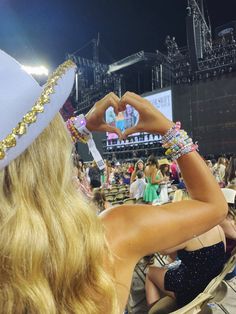 a woman in a white hat is making a heart with her hands at a concert