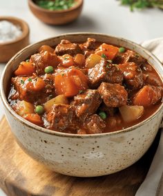 a bowl filled with meat and vegetables on top of a wooden cutting board next to other dishes