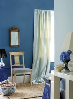 a blue and white living room with a chair, table, mirror and vases