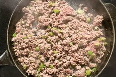 ground beef and green onions cooking in a skillet on top of the stovetop