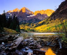 the mountains are covered in yellow and green leaves as they stand above a river with rocks