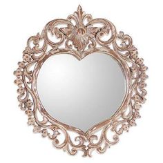 a heart shaped mirror hanging on the wall with an ornate frame and decorative details around it