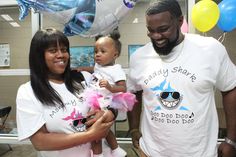 a man and woman holding a baby in front of balloons