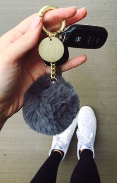 a person holding a cell phone and a keychain with a fur ball attached to it