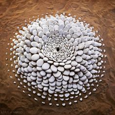 a large white flower made out of rocks on the ground with sand in the background