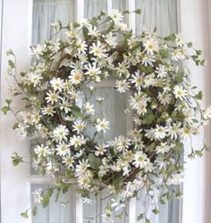 a wreath with daisies is hanging on a window sill in front of the door