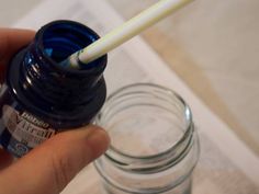 a hand holding a blue bottle with a white straw in it next to a glass jar