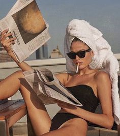 a woman with a towel on her head sitting on a bench and reading a newspaper