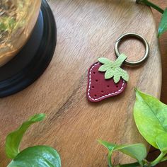 a strawberry shaped keychain sitting on top of a wooden table next to a potted plant