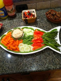 a fish shaped platter filled with veggies and dip