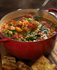 a red pot filled with vegetable soup next to crackers on a wooden table top