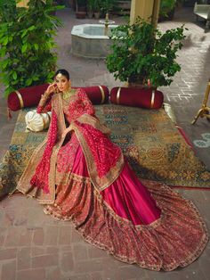 a woman in a red and gold bridal gown sitting on a rug with potted plants behind her