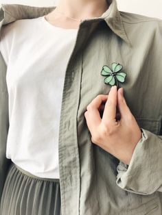 a woman wearing a white shirt holding a green clover brooch