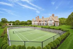 a tennis court in front of a large house with lots of trees and bushes around it